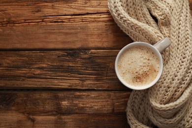 Photo of Top view of coffee and knitted scarf on wooden table, space for text. Cozy winter