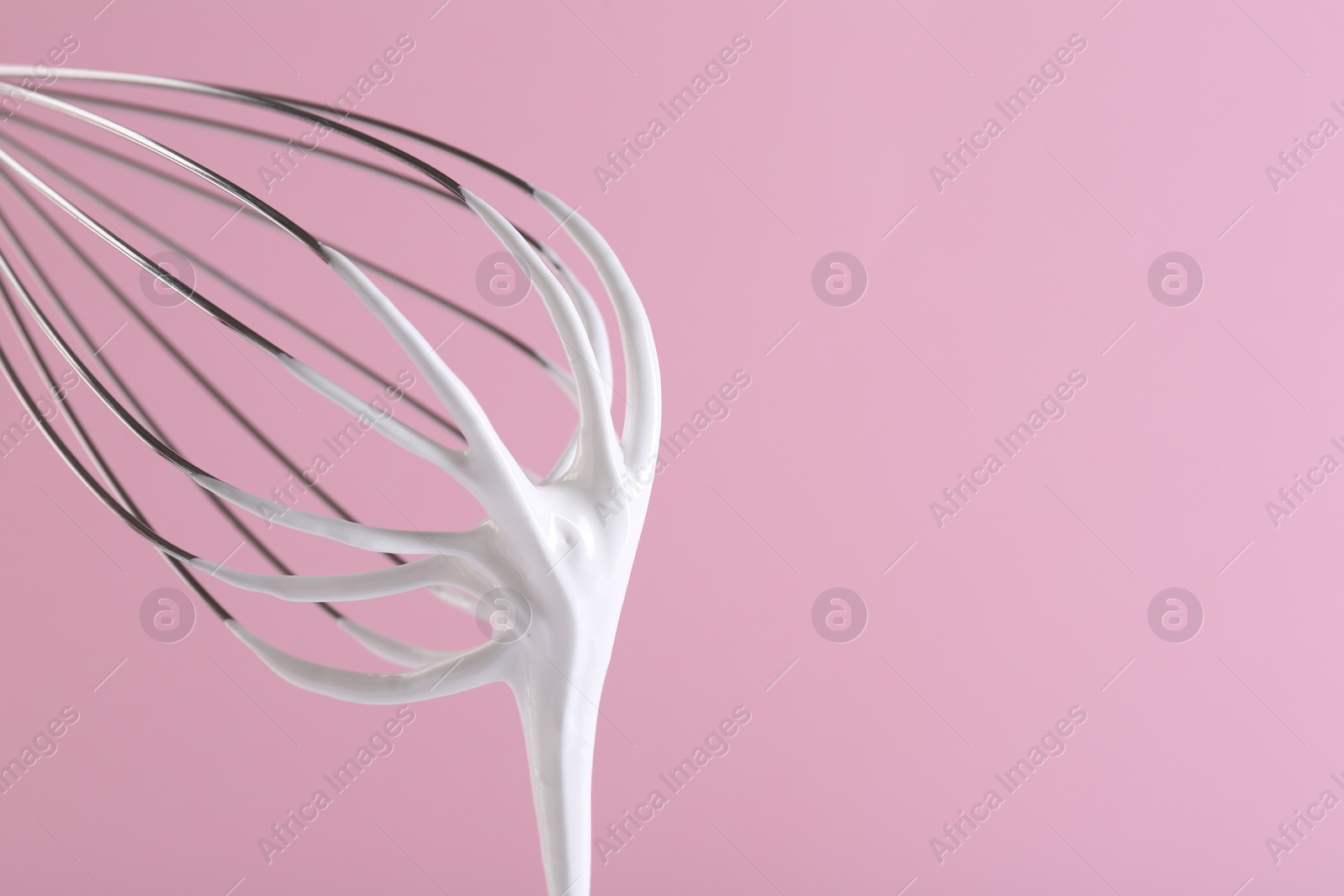 Photo of Whisk with whipped cream on pink background, closeup. Space for text