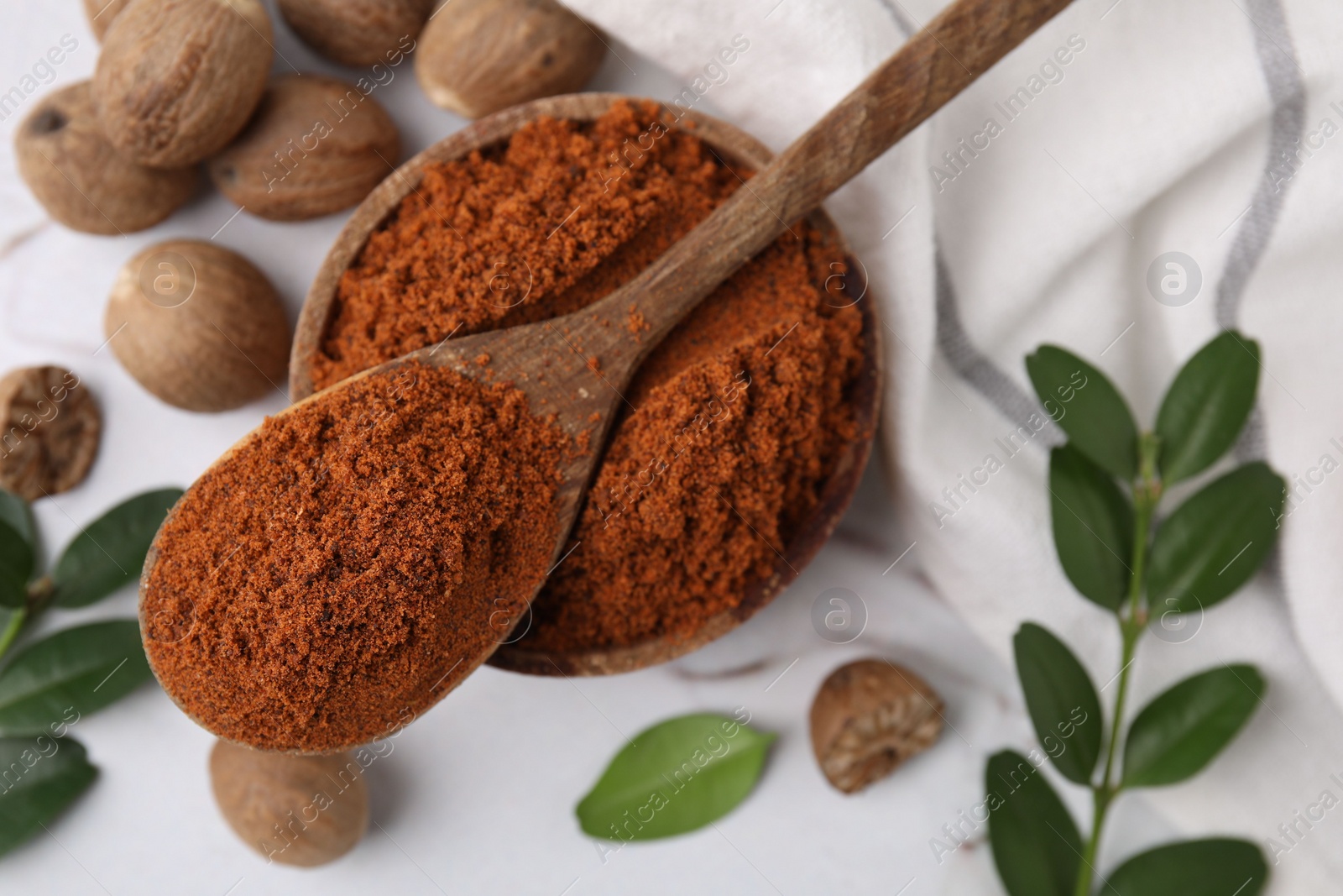 Photo of Nutmeg powder, seeds and green branches on white table, flat lay