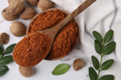 Nutmeg powder, seeds and green branches on white table, flat lay