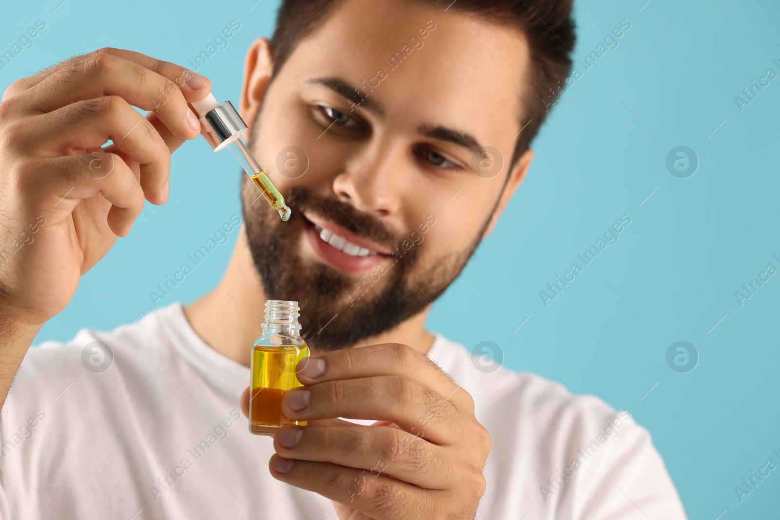 Photo of Handsome man with cosmetic serum in hands on light blue background, selective focus