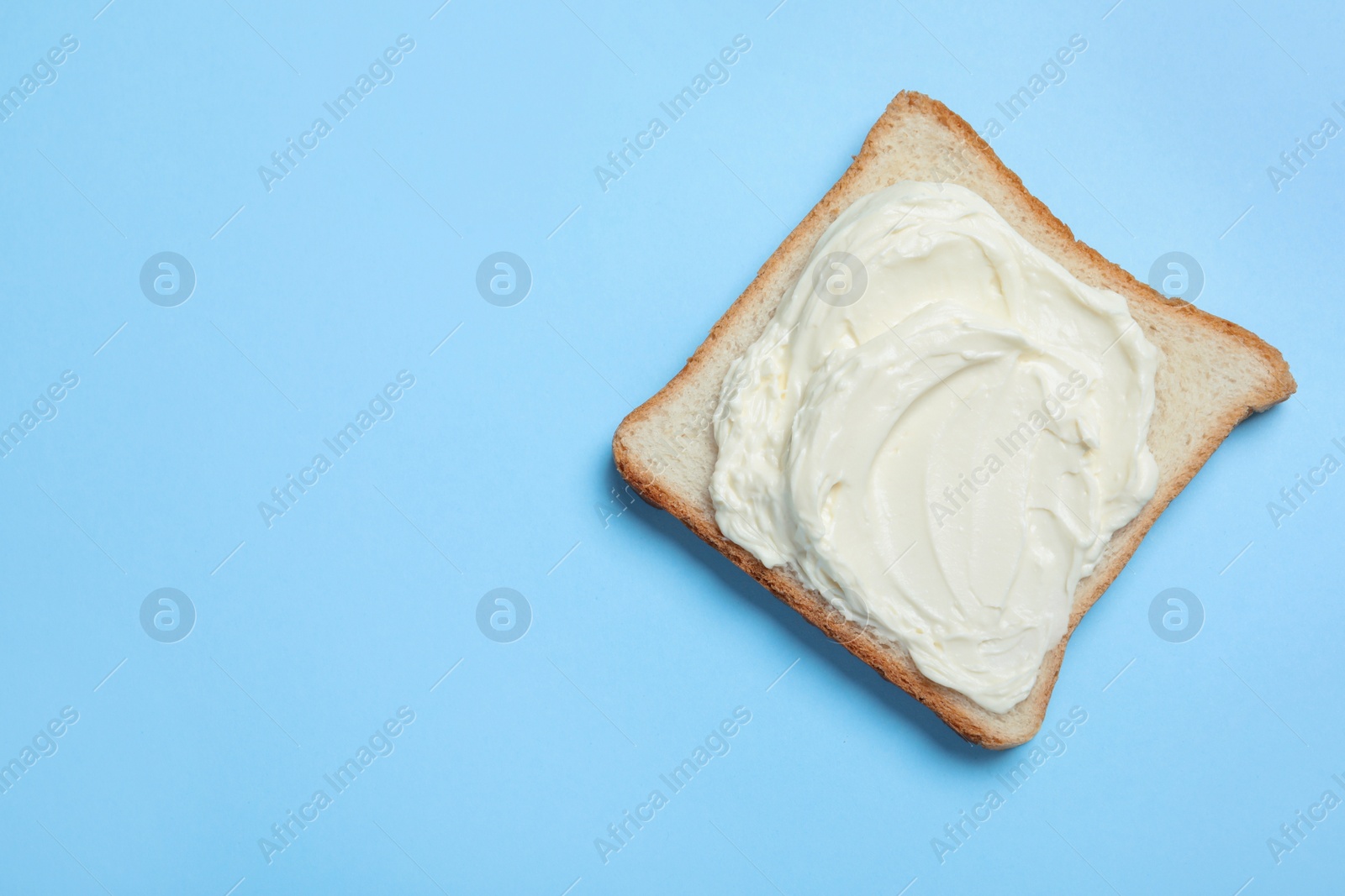 Photo of Slice of bread with tasty cream cheese on light blue background, top view. Space for text