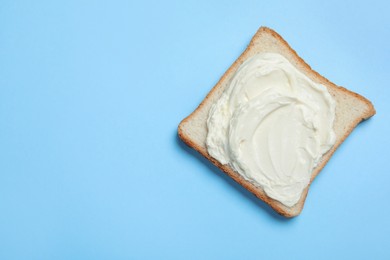 Photo of Slice of bread with tasty cream cheese on light blue background, top view. Space for text