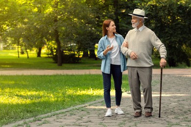 Photo of Senior man with walking cane and young woman in park. Space for text