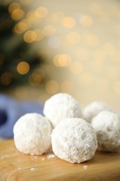 Photo of Christmas snowball cookies on wooden board against blurred lights, closeup