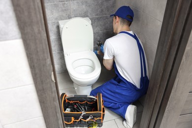 Photo of Plumber with spanner repairing toilet bowl in water closet