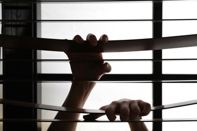 Woman holding on to window blinds, closeup. Stop violence