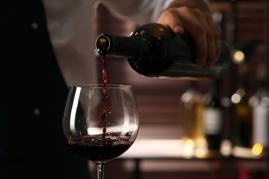 Bartender pouring red wine into glass indoors, closeup