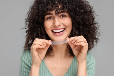 Young woman holding teeth whitening strip on grey background
