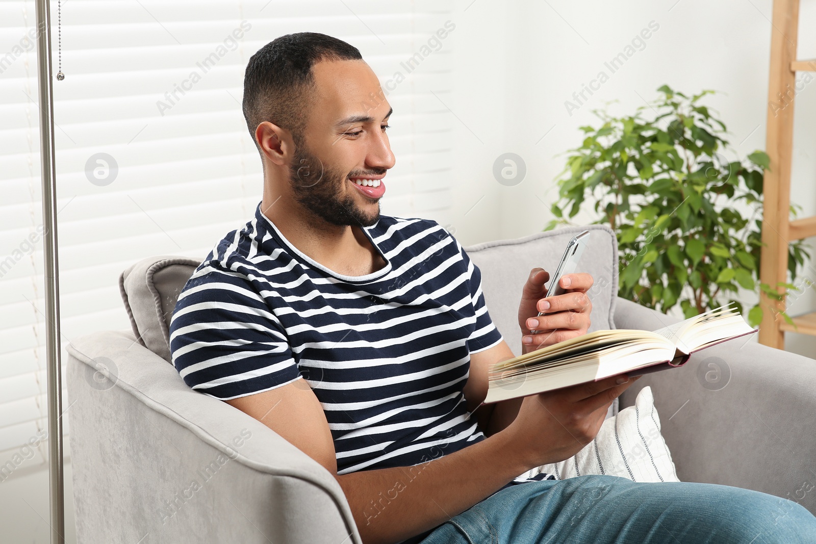 Photo of Happy man using smartphone while reading book at home. Internet addiction