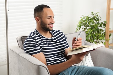 Happy man using smartphone while reading book at home. Internet addiction