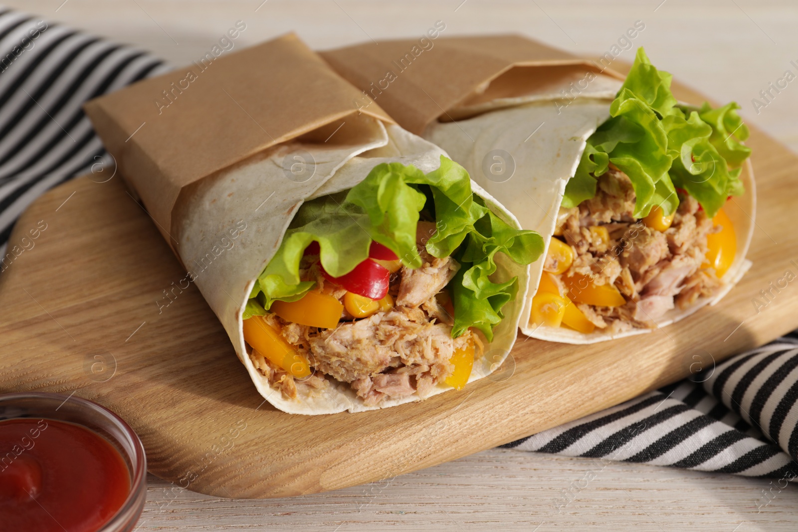 Photo of Delicious tortilla wraps with tuna on white wooden table, closeup