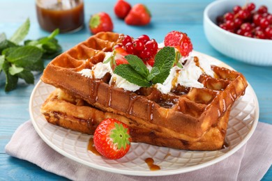 Delicious Belgian waffles with berries and caramel sauce served on turquoise wooden table, closeup