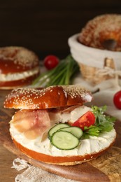 Photo of Delicious bagel with cream cheese, jamon, cucumber, tomato and parsley on wooden board