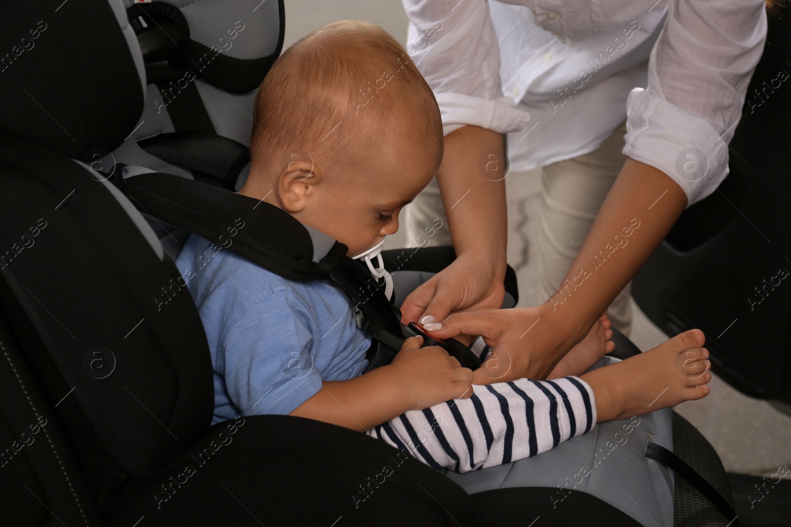 Photo of Mother fastening her son in child safety seat inside car