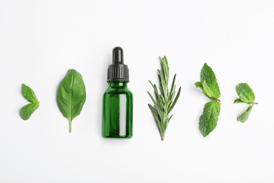 Little bottle of essential oil with different herbs on white background, top view