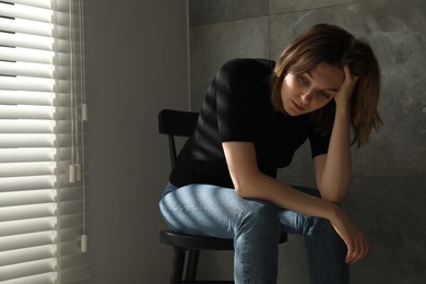 Photo of Sad young woman sitting on chair indoors, space for text