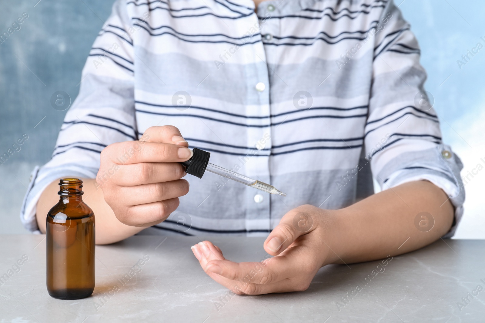 Photo of Woman dripping essential oil onto her hand at table, closeup