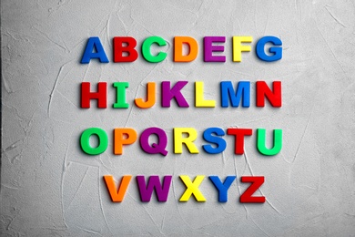 Colorful magnetic letters on light grey stone background, flat lay. Alphabetical order