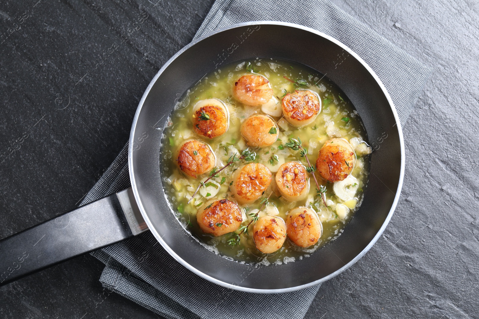 Photo of Delicious scallops with sauce in frying pan on dark gray textured table, top view