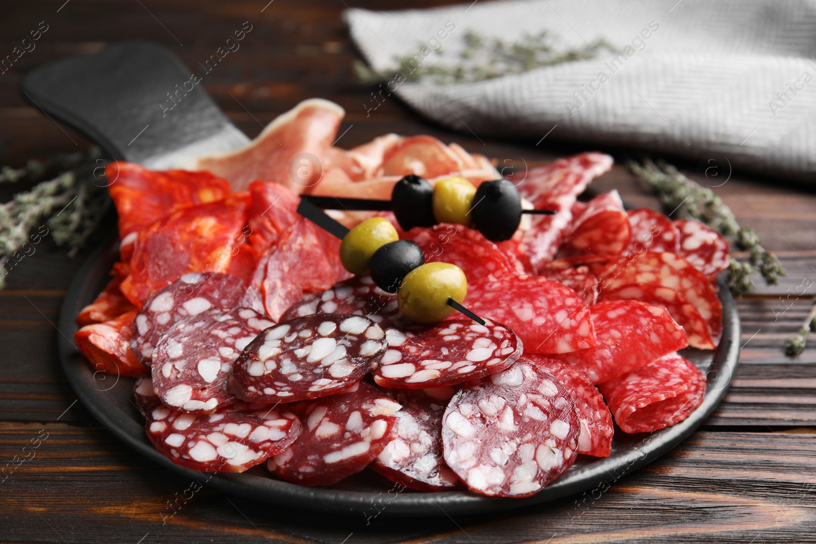 Photo of Tasty salami and other delicacies on wooden table, closeup