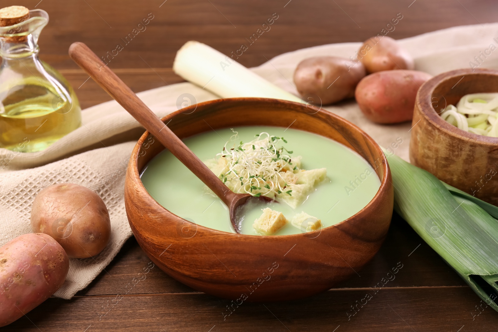 Photo of Bowl of tasty leek soup, spoon and ingredients on wooden table