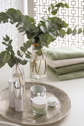 Fresh eucalyptus branches and cosmetic products on countertop in bathroom