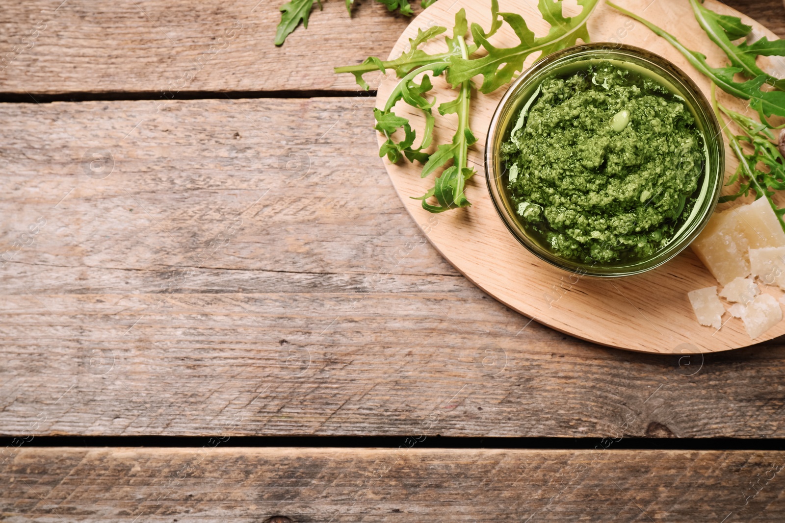 Photo of Bowl of tasty arugula pesto and ingredients on wooden table, flat lay. Space for text