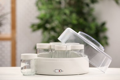 Photo of Modern yogurt maker with empty jars on white table indoors