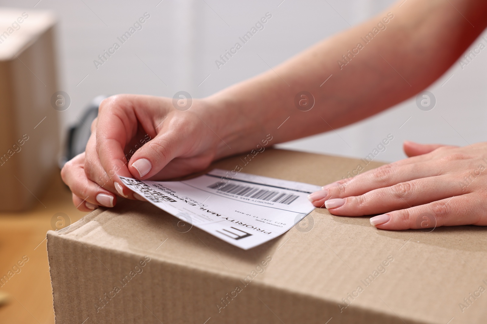 Photo of Parcel packing. Post office worker sticking barcode on box indoors, closeup