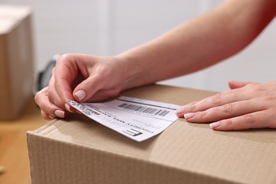 Photo of Parcel packing. Post office worker sticking barcode on box indoors, closeup