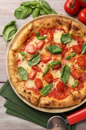 Delicious Margherita pizza and cutter on wooden table, flat lay