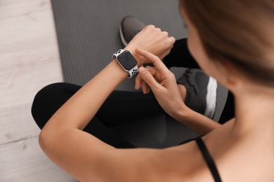 Photo of Young woman using smart watch during training indoors, closeup
