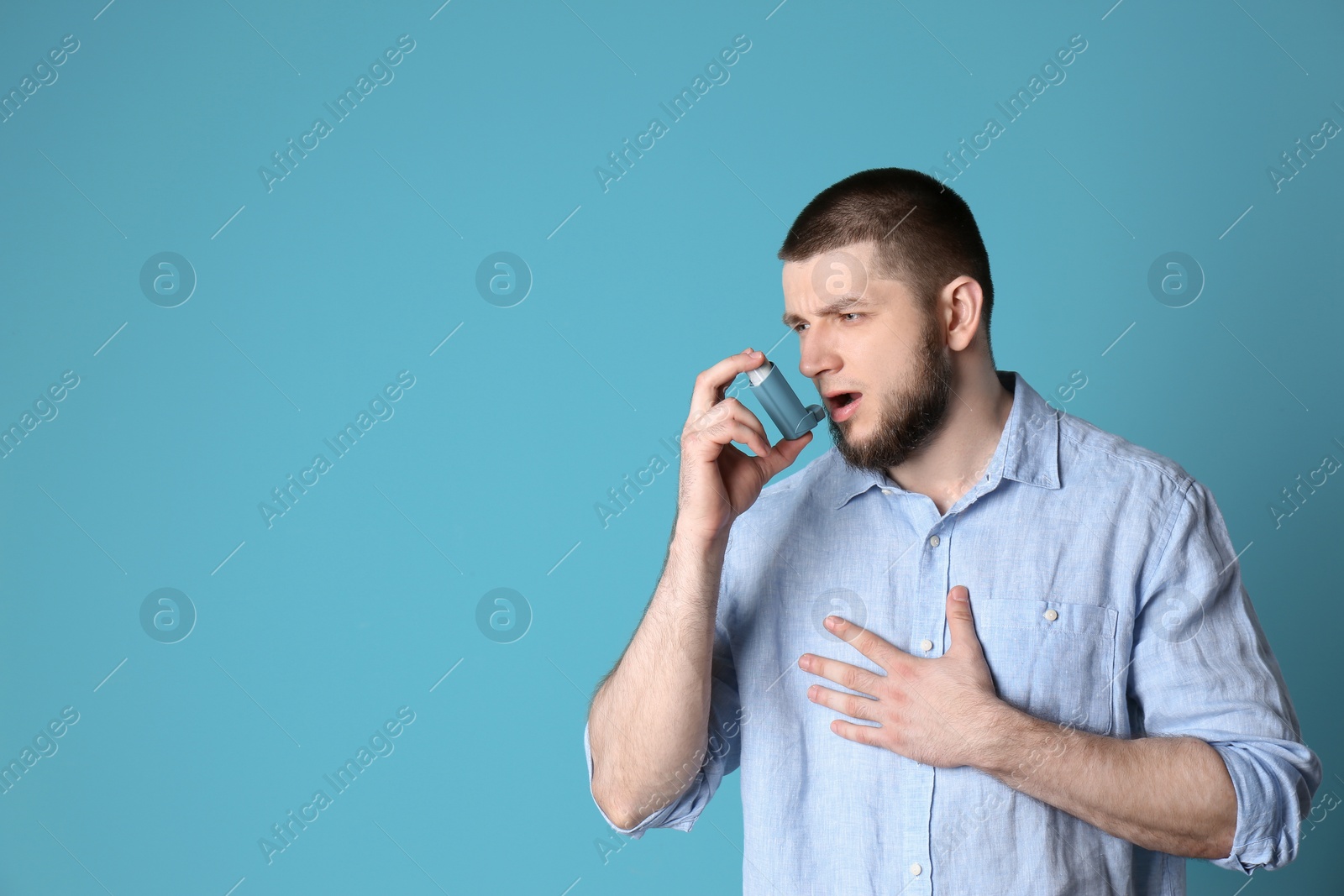 Photo of Young man using asthma inhaler on color background with space for text