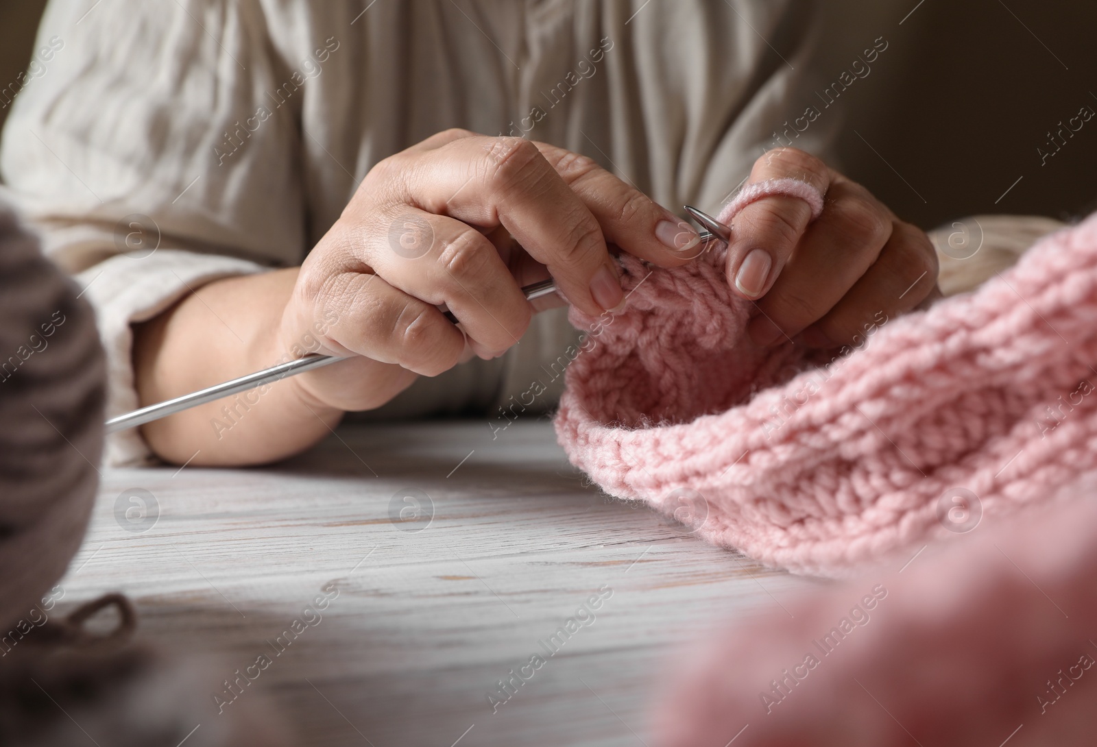 Photo of Woman knitting at white wooden table, closeup. Creative hobby