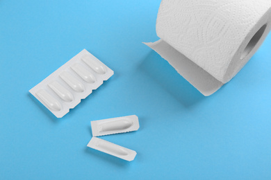 Photo of Suppositories and toilet paper on light blue background, flat lay. Hemorrhoid treatment