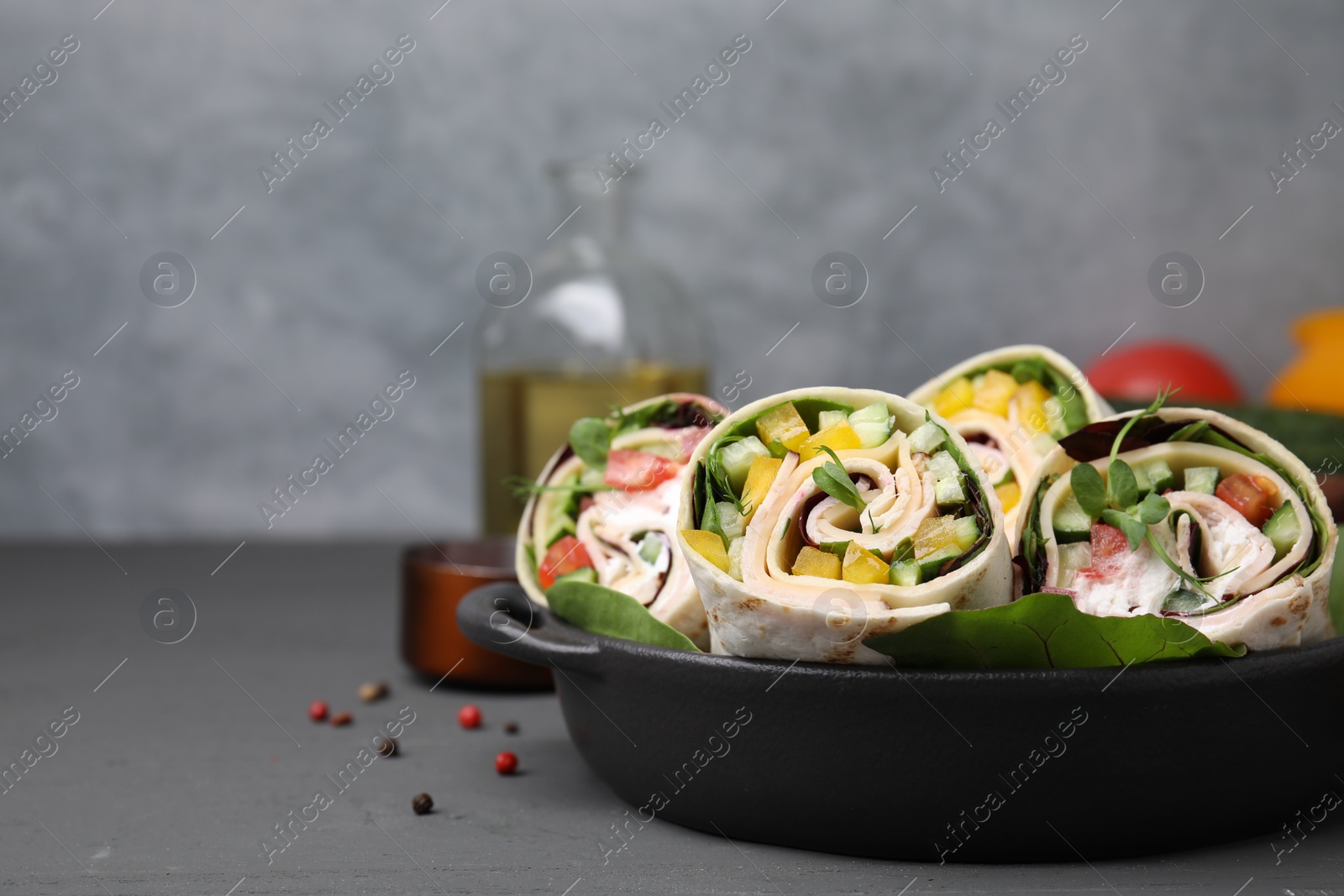 Photo of Delicious sandwich wraps with fresh vegetables on grey table, closeup. Space for text