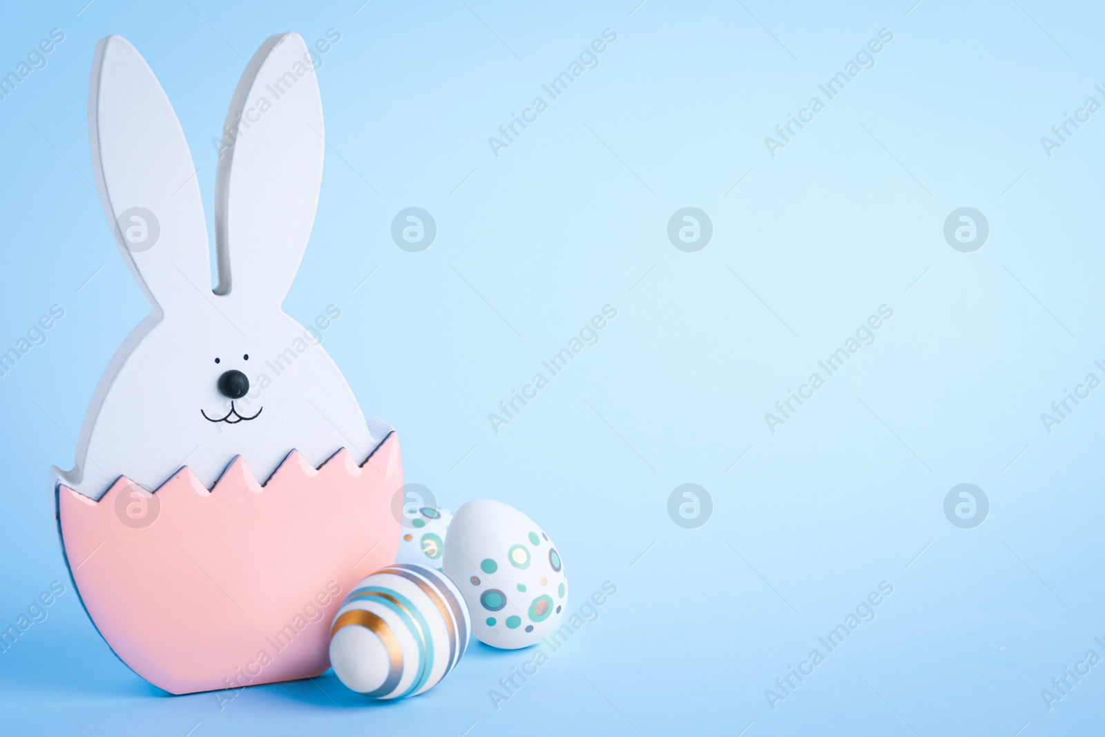 Photo of Easter bunny figure and decorated eggs on light blue background. Space for text