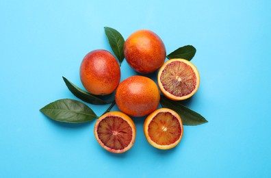 Photo of Many ripe sicilian oranges and leaves on light blue background, flat lay