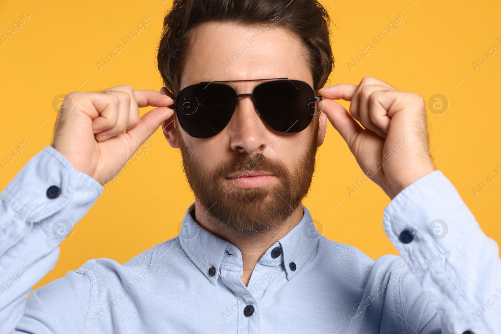 Photo of Portrait of bearded man with stylish sunglasses on orange background, closeup