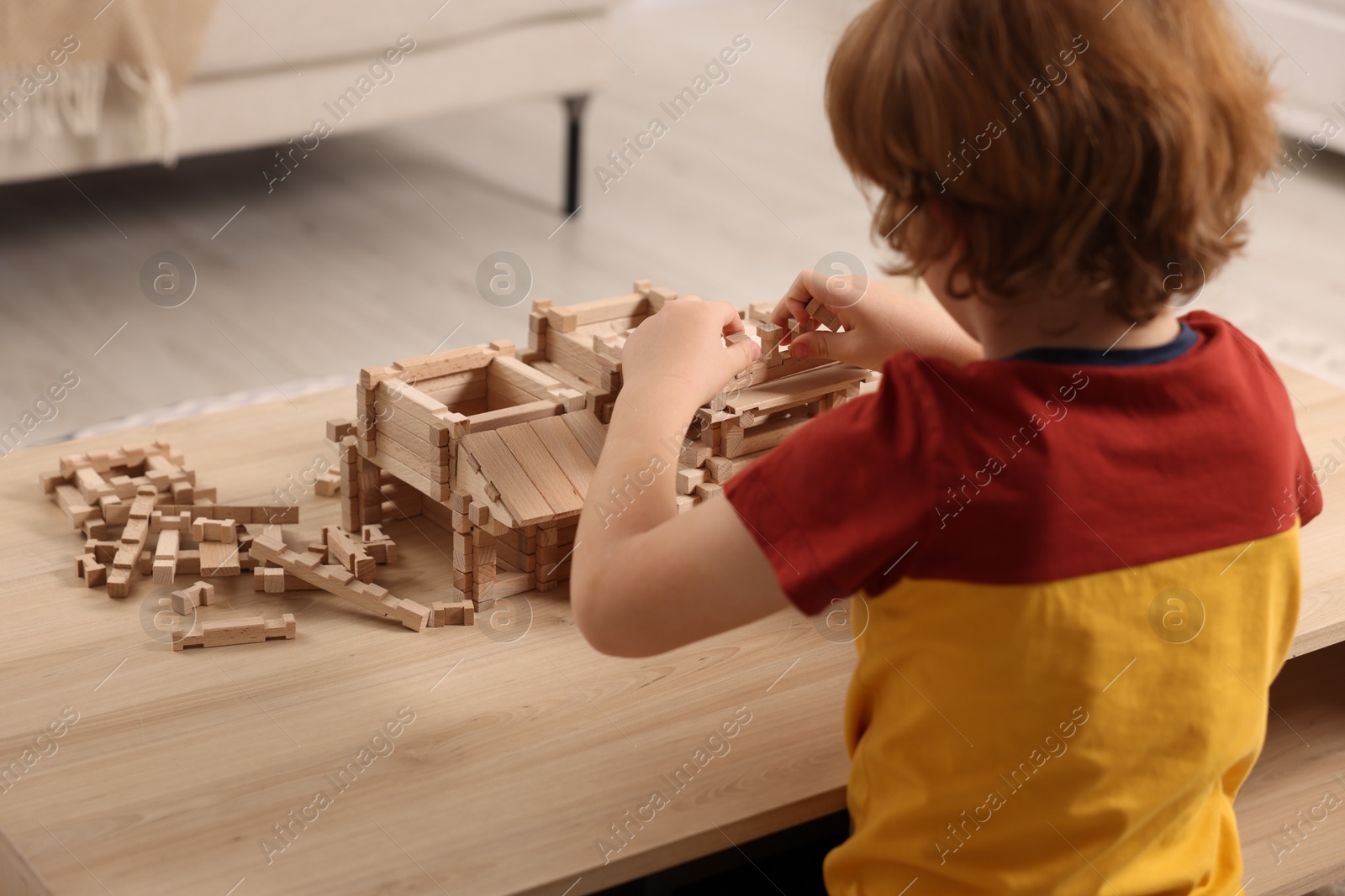 Photo of Little boy playing with wooden construction set at table in room. Child's toy