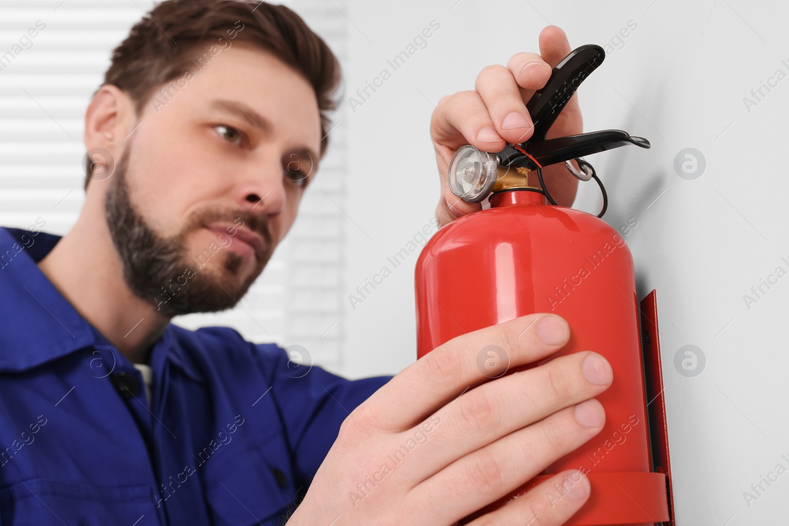 Photo of Man checking fire extinguisher indoors, selective focus