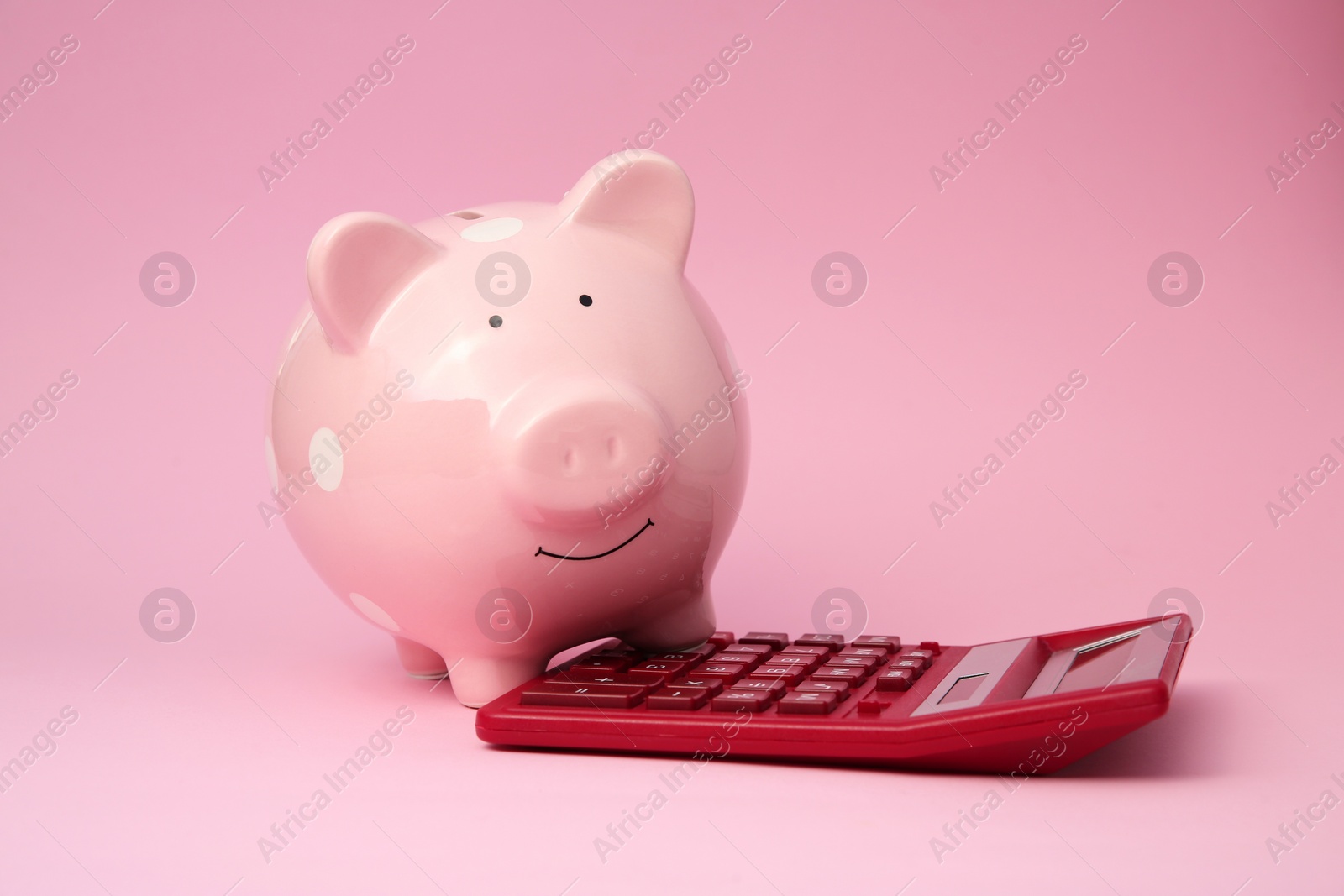 Photo of Piggy bank and calculator on pink background
