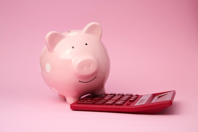 Piggy bank and calculator on pink background