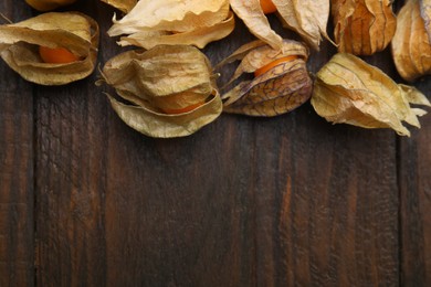 Ripe physalis fruits with calyxes on wooden table, flat lay. Space for text