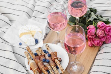 Glasses of delicious rose wine, flowers and food on white picnic blanket