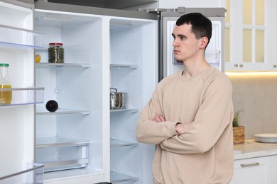 Photo of Upset man near empty refrigerator in kitchen