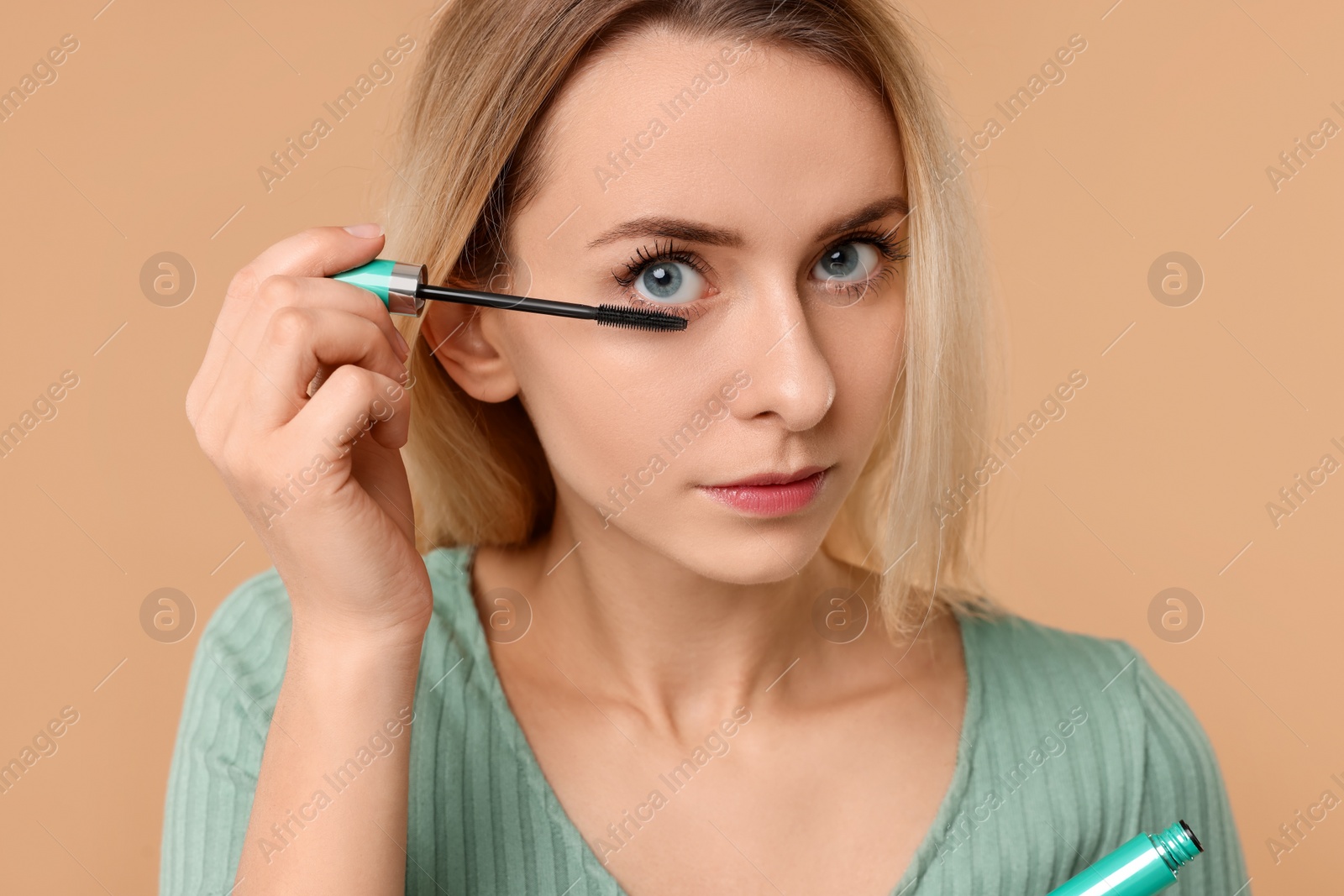 Photo of Beautiful woman applying mascara on beige background, closeup