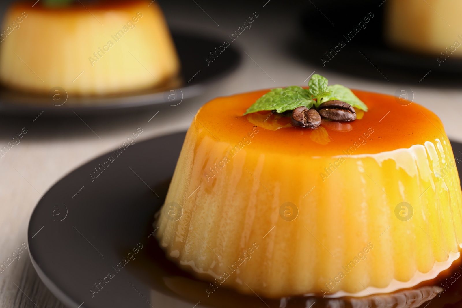 Photo of Plate of delicious caramel pudding with coffee beans and mint on table, closeup