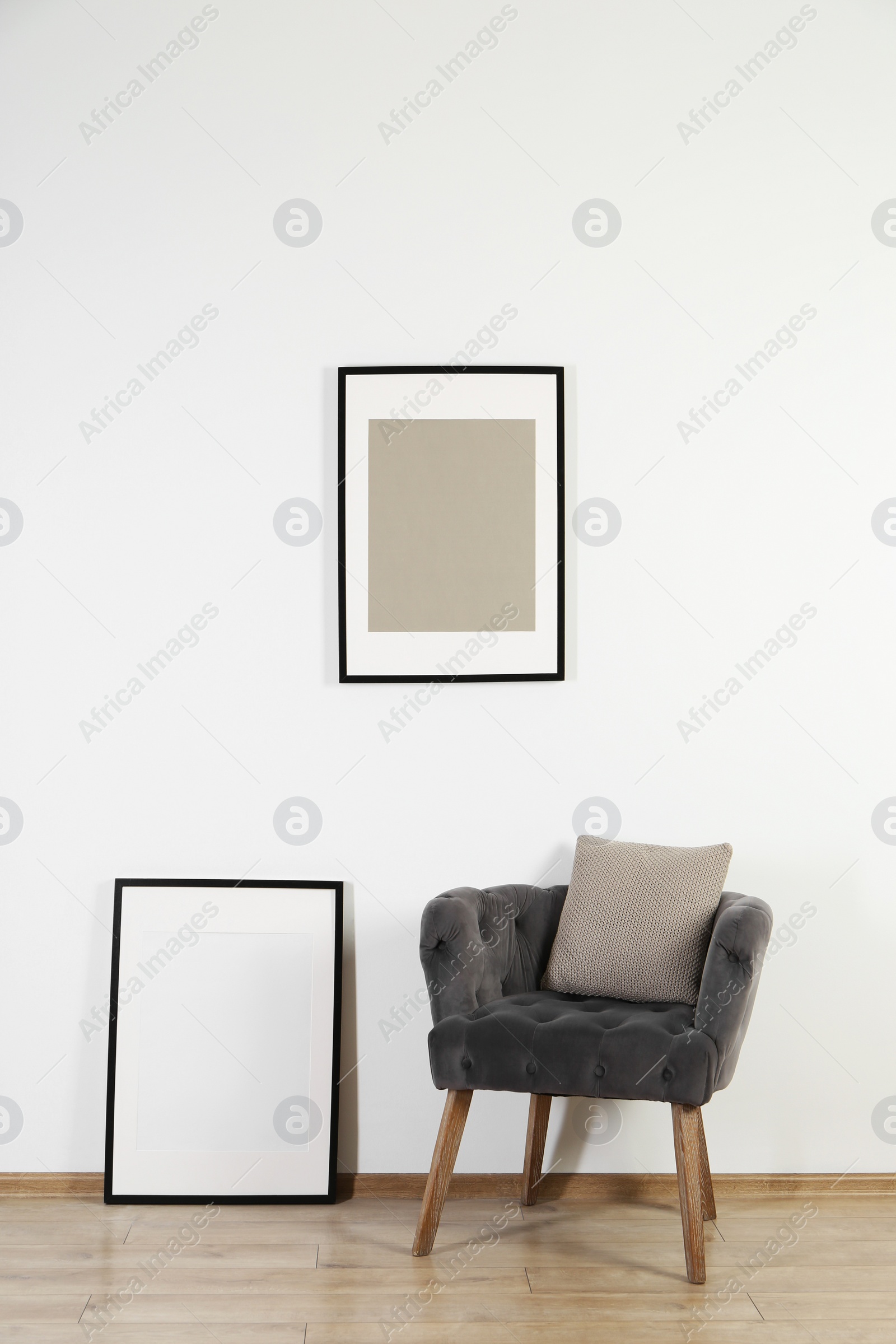 Photo of Comfortable armchair, cushion and frames in room with white wall. Interior design